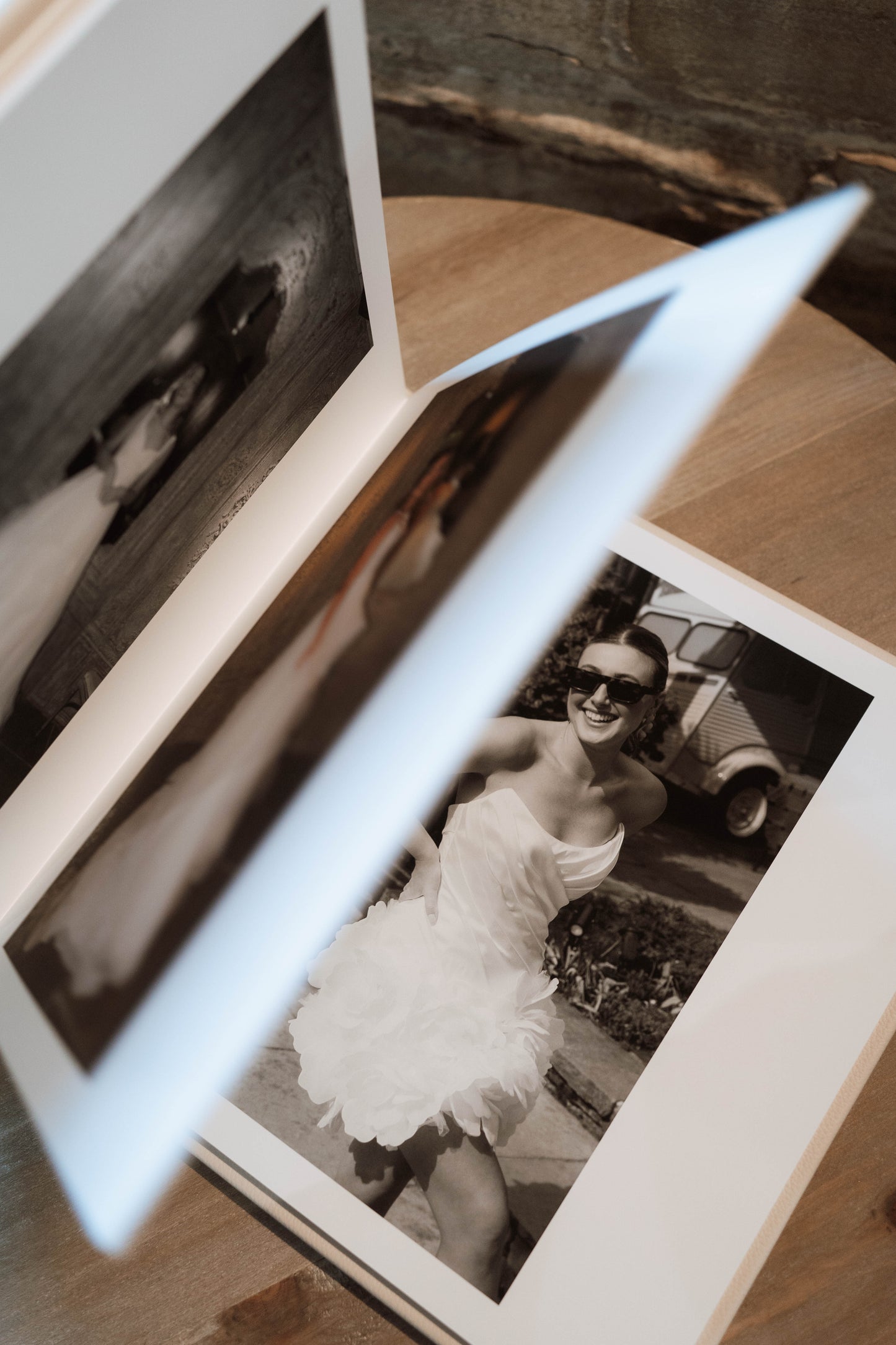 An open photo album or book lying on a wooden surface, with pages fanned open to reveal black-and-white printed photographs inside.
