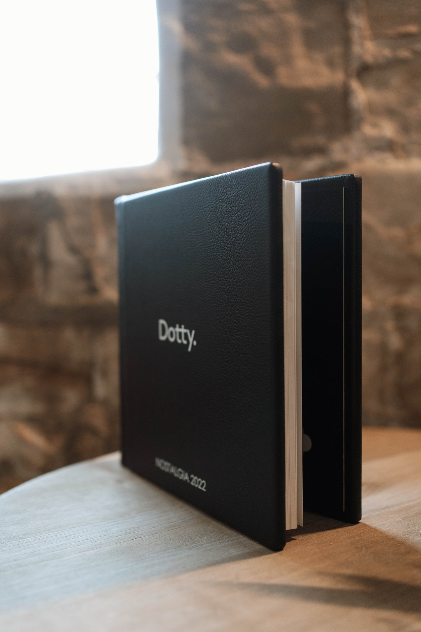 A black leather hardcover wedding albums standing upright on a wooden table, with the word 'Dotty.' printed in white on the cover and 'MOSCOW 2022' near the bottom.