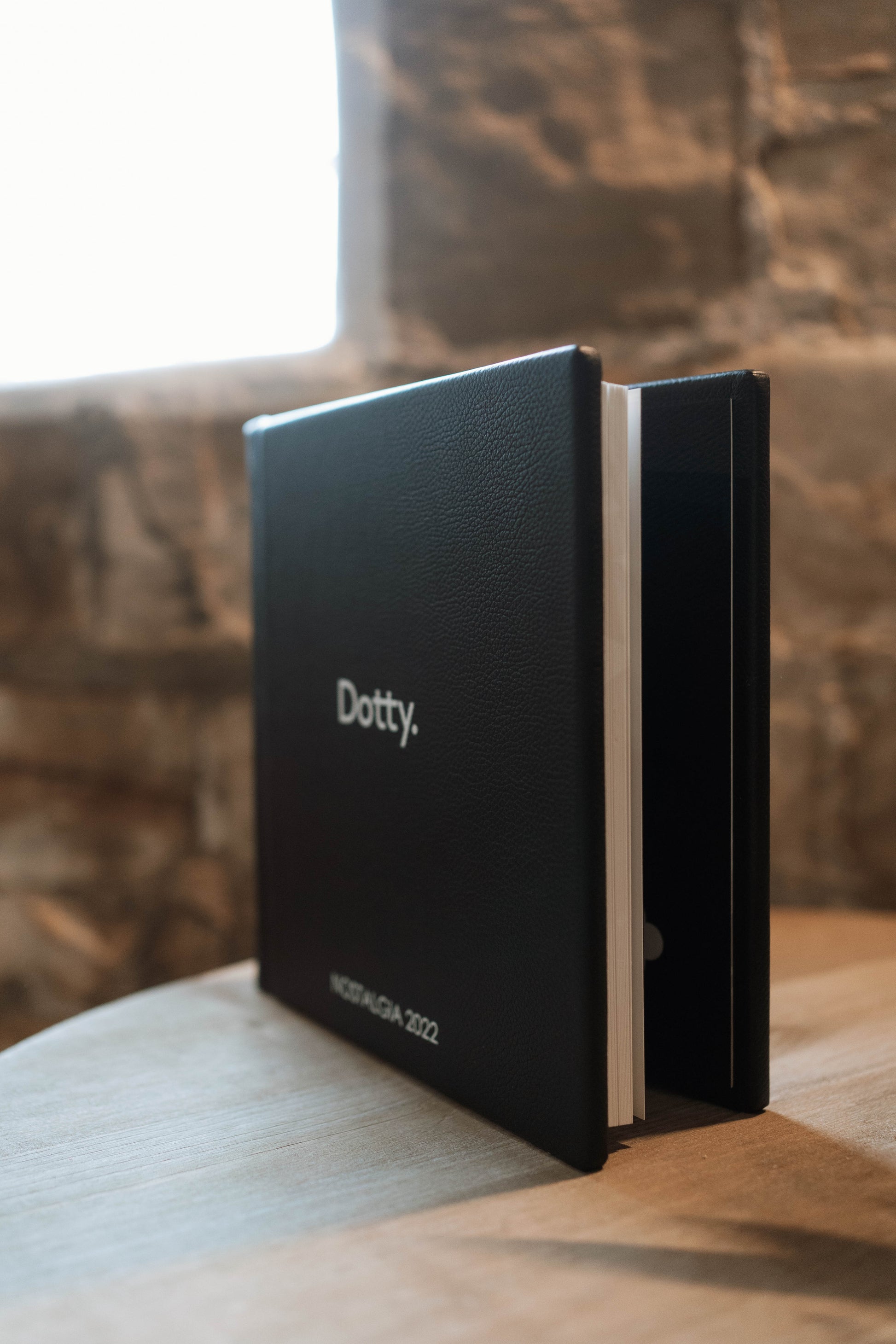 A black leather hardcover wedding albums standing upright on a wooden table, with the word 'Dotty.' printed in white on the cover and 'MOSCOW 2022' near the bottom.